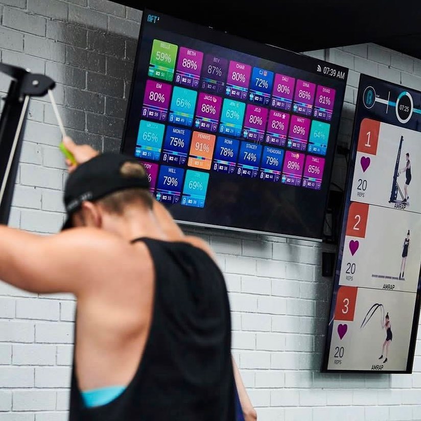 A member training while the heart rate leaderboard and workout screens run above